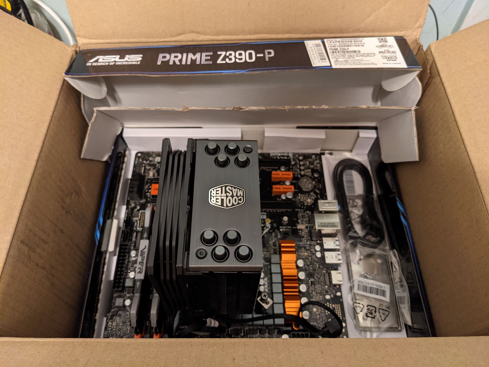 An open ASUS Prime Z390-P motherboard box with a motherboard and a Cooler Master tower cooler inside.