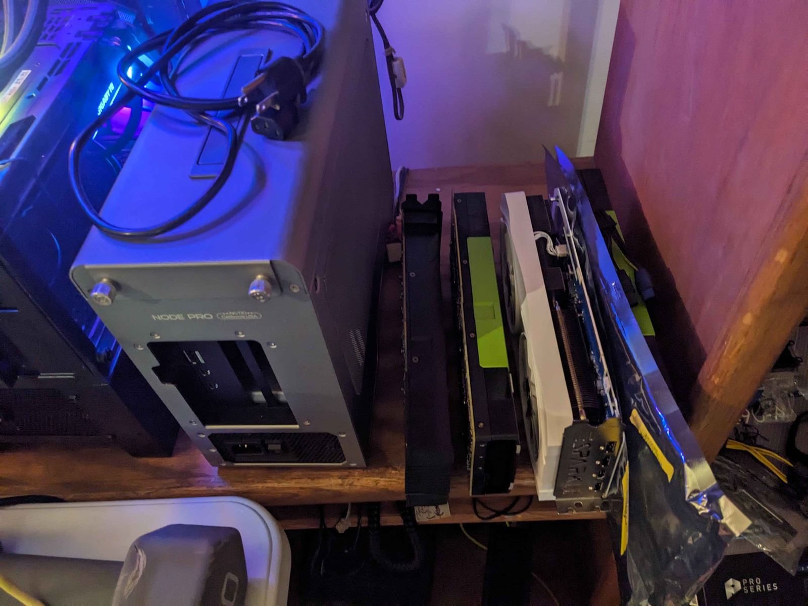 A Node Pro enclosure beside a row of graphics cards standing on a wooden shelf.