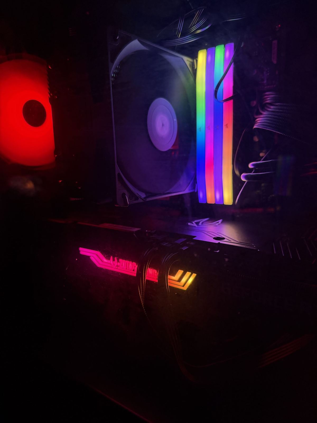 Inside a dark PC case: four RGB memory modules, a cooler fan, a red-lit fan and a graphics card with a glowing Zotac Gaming logo.